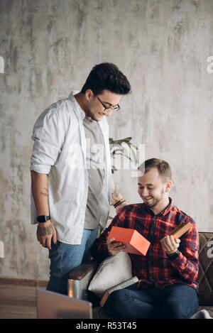 Happy surprised young handsome gay couple celebrating and giving gift at home Stock Photo