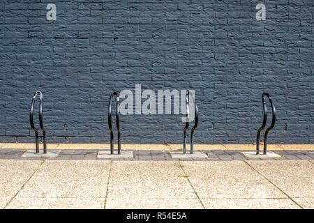 Very simple bike, bicycle racks, painted black in front of a black brick wall. Stock Photo