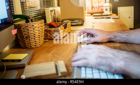 close-up of a man sitting at the desk and typing on the keyboard of his desktop computer in the evening in the home office Stock Photo