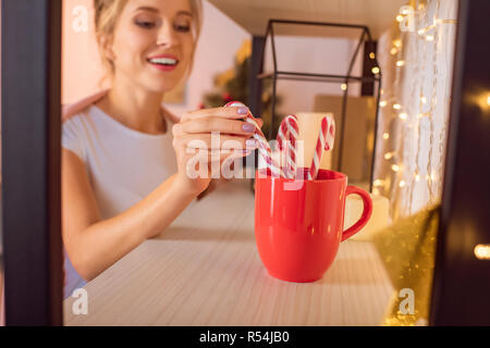 smiling young blonde woman putting candy canes in red cup at christmas time Stock Photo