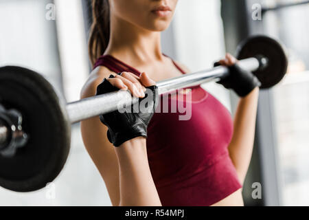 cropped view of concentrated sportswoman in weight lifting gloves training with barbell at gym Stock Photo