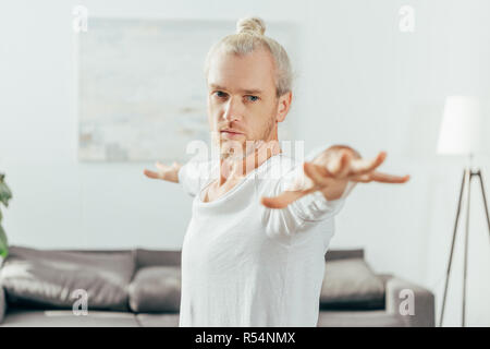 concentrated adult man standing in warrior yoga pose at home Stock Photo