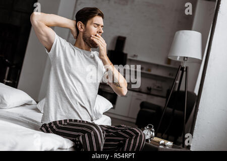 young man in pajamas yawning and stretching on bed in the morning Stock Photo