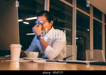 businessman looking tired working late night in office. Man sitting in front of computer working late looking stressed out. Stock Photo
