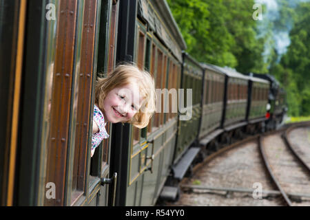 Passenger young girl aged 8 / eight years old, smiling & looking out of the window of a moving train carriage on the Isle of Wight steam Railway line. UK. (98) Stock Photo