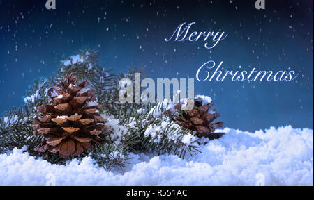Snow covered pine cones and evergreen tree branches with Merry Christmas text against a winter night sky Stock Photo