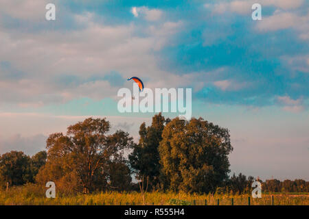 Motorized paraglider flying in rural area during sunset Stock Photo