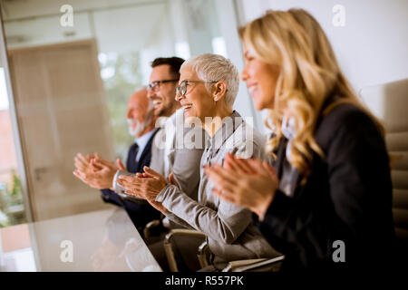 Satisfied proud business team clapping hands while sitting in row at office Stock Photo