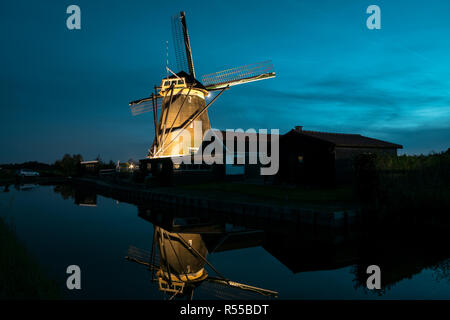A classic dutch windmill at the river Rotte near Zevenhuizen is illuminated by lights at blue hour. Beautiful reflections of the windmill in the water Stock Photo