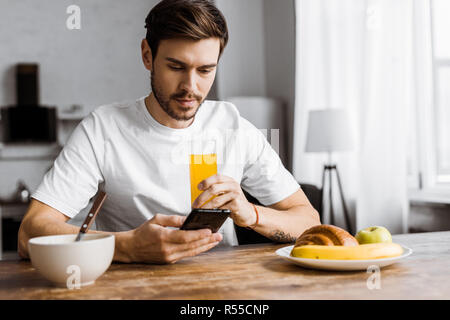 handsome young man using smartphone during breakfast at home Stock Photo