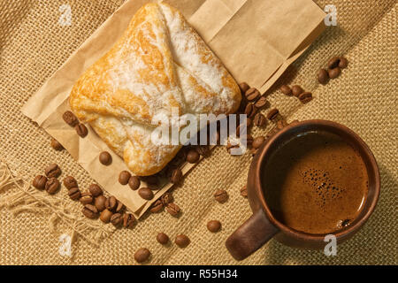 Top view of a cup of coffee with foam and bun on an old burlap and craft paper with a coffee beans Stock Photo