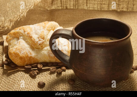 Top view of a cup of coffee with foam and bun on an old burlap and craft paper with a coffee beans Stock Photo