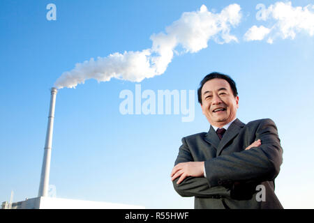 Businessman in Front of Smokestack Stock Photo