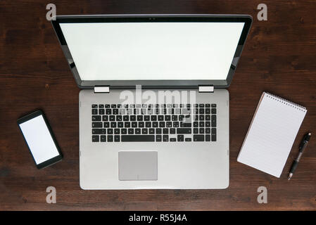 Top view of laptop on desk with smartphone and notepad, dark brown wooden workspace concept Stock Photo