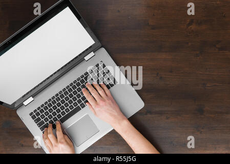 Top view of man working on laptop computer on brown wooden desk Stock Photo