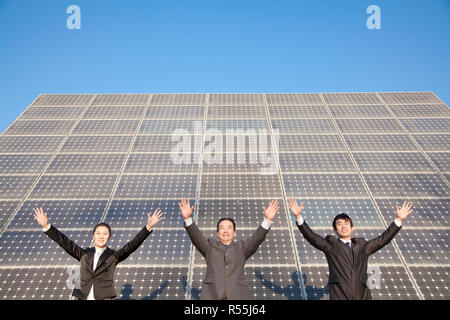 Businesspeople with Arms Outstretched in front of Solar Panel Stock Photo