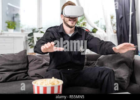 police officer with virtual reality headset on head sitting on couch and playing video game Stock Photo