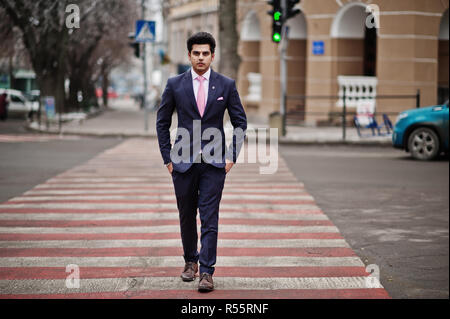 Elegant indian macho man model on suit and pink tie walking at cross pedestrian. Stock Photo