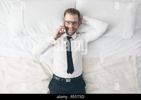 Top view. Handsome businessman with glasses on bed calling from his phone Stock Photo
