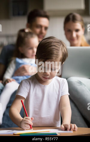 Little boy drawing while parents playing with daughter Stock Photo