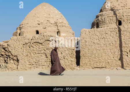 Local Arabian Egyptian man walking dressed in national male dress thawb (thobe) by ancient islamic sheikh mausoleum. Old town Al Qasr, Dakhla, Egypt. Stock Photo