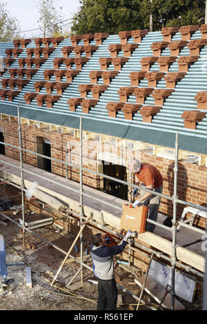 Buckingham, UK - November 03, 2016. Roofers work on a new build. Clay tiles are stacked on the roof battens ready for tiling Stock Photo