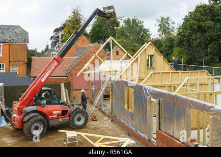 Buckingham, UK - October 13, 2016. Heavy machinery lifts a roof truss into place on an extension to a period house. The extension is of timber frame c Stock Photo