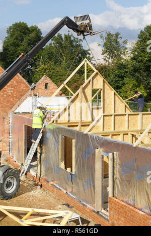 Buckingham, UK - October 13, 2016. A builder at work on a building site in the UK installs roof trusses to a timber frame house extension Stock Photo