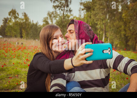 Couple doing silly and funny faces while taking selfie picture with their mobile phone in field of red poppies Stock Photo