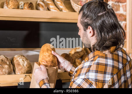 Male seller putting fresh bread in paper bag Stock Photo