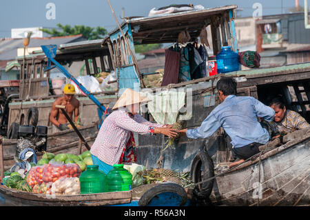 Female boatwoman selling produce hands over a pineapple to a buyer on another wooden boat at the Cai Rang Floating Market, Can Tho Province,Vietnam Stock Photo