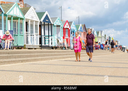 Southwold, UK - September 6, 2018 - A couple walking on the promenade in Southwold with a row of beach huts in the background Stock Photo