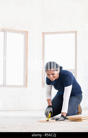 A female builder measuring a plank of wood Stock Photo