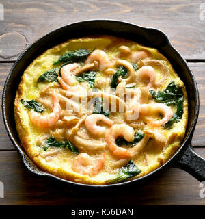 Omelette with mushroom, spinach and  shrimps in frying pan on wooden table Stock Photo