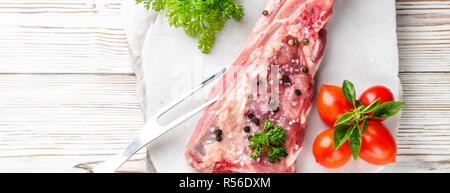 Piece of meat pork brisket ribs spatula seasoned with salt pepper cherry tomato and sprig of basil parsley on white wooden table marble stone served w Stock Photo