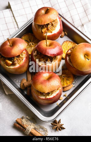 Baked apples with granola, cinnamon, nuts and honey on stone background. Healthy fruit dessert. Stock Photo