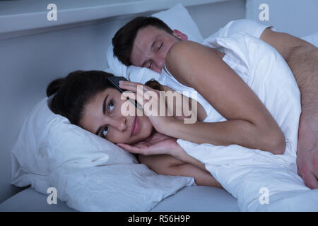 Woman Using Mobile Phone While Husband Sleeping Stock Photo