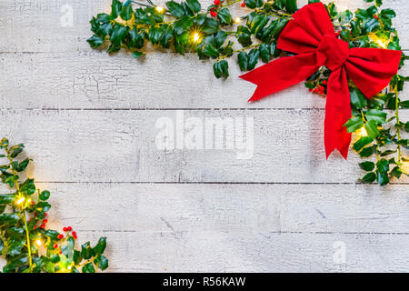 Christmas holly with bow, lights and berries on a white wood background Stock Photo