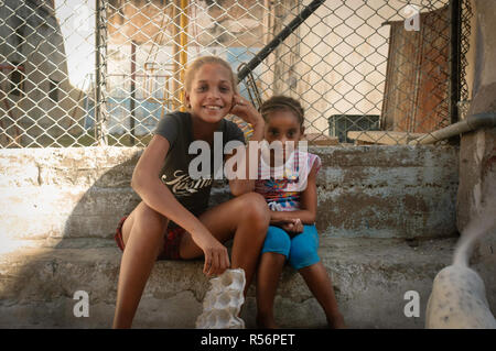 Smiling young Cuban girls sitting on a wall with their dog. Havana, Cuba Stock Photo
