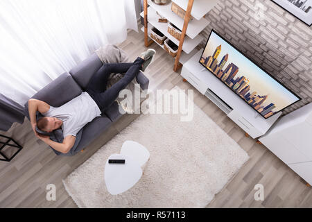 High Angle View Of A Young Man Relaxing On Sofa Watching Television Stock Photo