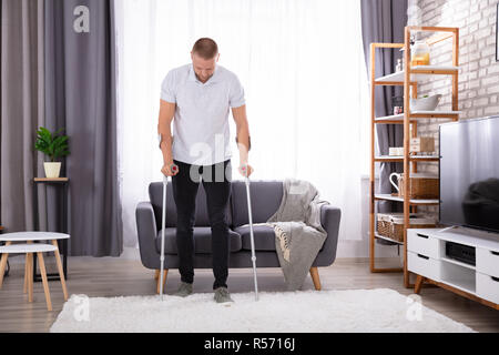 Disabled Young Man Using Crutches To Walk On Carpet Stock Photo