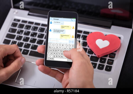Man Sending Text Message On Mobile Phone With Red Heart Over Laptop Stock Photo