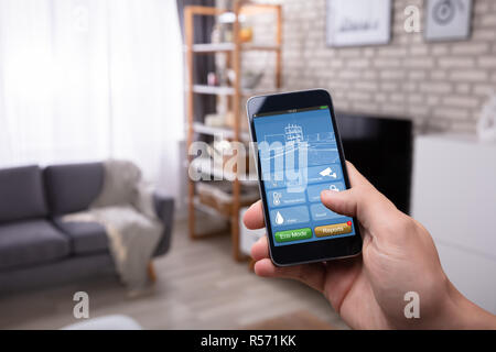 Close-up Of A Man's Hand Using Smart Home Application On Mobile Phone At Home Stock Photo