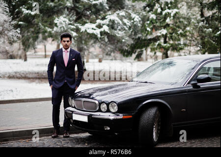 Elegant indian macho man model on suit and pink tie posed against black classic car. Stock Photo