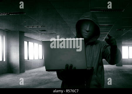 Hacker man with anonymous mask holding laptop while standing Stock Photo