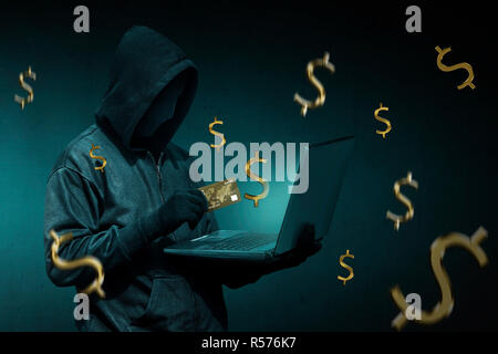 Hooded hacker with credit card stealing data from a laptop Stock Photo