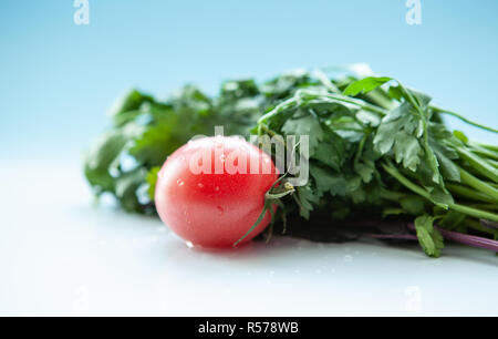 Juicy tomato and dill with parsley on a light blue background, close-up Stock Photo