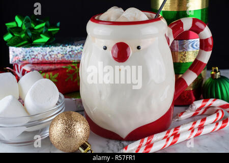 Santa Claus Mug with Hot Chocolate & Marshmellows with Candy Canes and Peppermint Sticks Presents Satin Bows and Fresh Marsh mellows Stock Photo