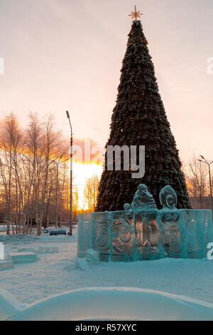 Santa Claus and snow Maiden cut out of ice on the background of the Christmas tree in the rays of the setting sun Stock Photo