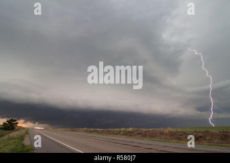 A lightning bolt arcs out of a supercell thunderstorm, striking the ground. Stock Photo